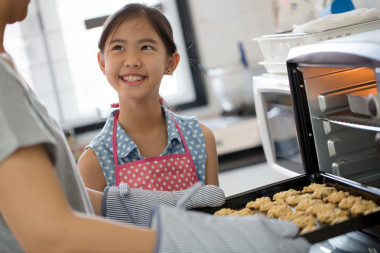 快乐小亚洲可爱厨师从烤箱看饼干