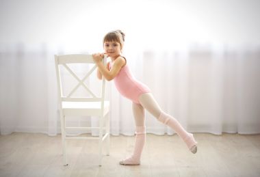 可爱的小女孩在舞蹈工作室制作新芭蕾运动椅边的粉红色紧身连衣裤