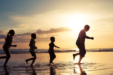 父親和孩子們在日落的時候在海灘上玩