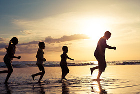 父亲和孩子们在日落的时候在海滩上玩