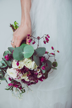 与在她手中的鲜花合影时穿白色的礼服婚纱新娘的画像。在新娘的手的美丽婚礼花束