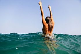 性感的女孩游泳海波浪举起手来溅后视图
