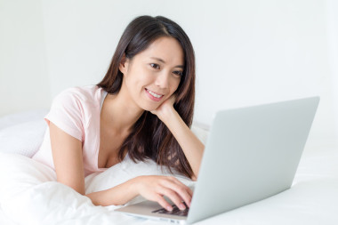 使用便攜式計(jì)算機(jī)和躺在床上的女人