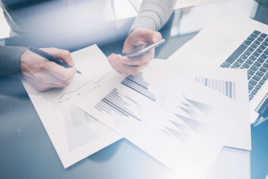 照片客户经理在餐桌上处理新的业务项目。握着现代智能手机的手，统计屏幕。签署文档并分析计划。水平，模糊，胶片效果