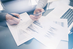 照片客户经理在餐桌上处理新的业务项目。握着现代智能手机的手,统计屏幕。签署文档并分析计划。水平,模糊,胶片效果