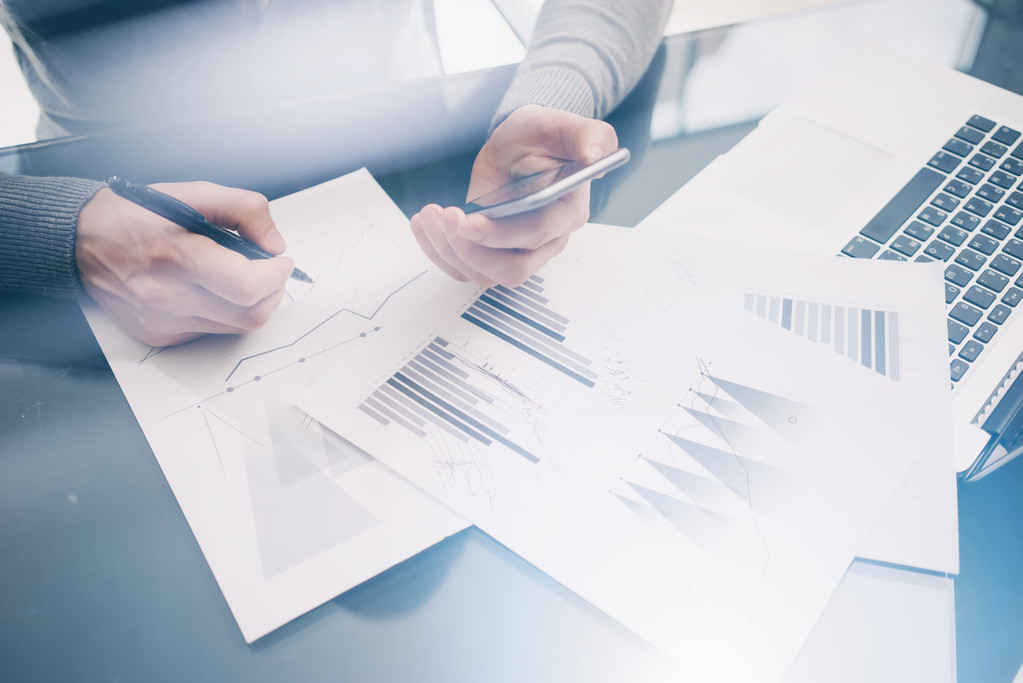 照片客户经理在餐桌上处理新的业务项目。握着现代智能手机的手,统计屏幕。签署文档并分析计划。水平,模糊,胶片效果 照片客户经理在餐桌上处理新的业务项目。握着现代智能手机的手,统计屏幕。签署文档并分析计划。水平,模糊,胶片效果