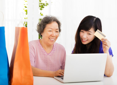 快樂的高級母親和女兒與筆記本電腦和信用卡  