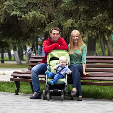 年轻的父母坐在一张长椅上,他年轻的儿子 年轻的父母坐在一张长椅上,他年轻的儿子