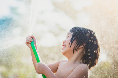 可愛(ài)的亞洲男孩已玩戶外軟管從水中