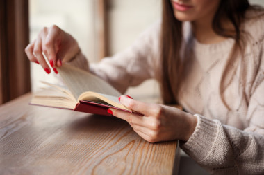 女孩拿著一本書穿著溫暖的羊毛拉扯與紅色凝膠拋光美甲。木材復(fù)古背景。學(xué)生女性概念