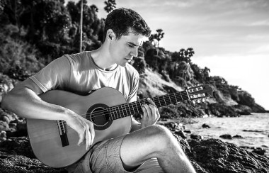 帥氣的微笑吉他手玩音樂選址上海灘巖。黑色白色戶外寫真