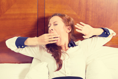 昏昏欲睡的年輕商業(yè)婦女打哈欠躺在床上試圖醒來