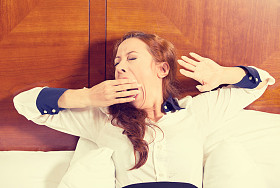 昏昏欲睡的年轻商业妇女打哈欠躺在床上试图醒来