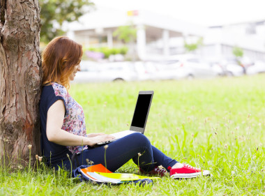 女学生在使用笔记本电脑的草地上 