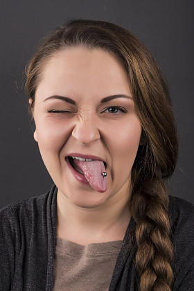 女孩在灰色的背景上显示的舌头。穿甲的情绪