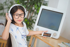 迷人的亚洲女孩在智能手机与耳机在房间里听音乐