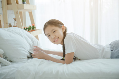 快樂美麗的亞洲女孩躺在床上時使用平板電腦