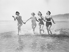 四名妇女在海滩上在水中运行照片
