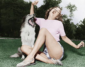 年轻女子坐在草坪上，唱歌与她的狗