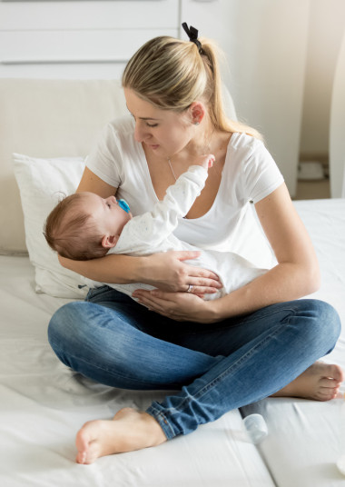 年輕的媽媽坐在床上和她 3 個月大男嬰