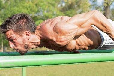 在室外的健身房鍛煉的年輕運動員。街頭的健身運動。緊張的肌肉