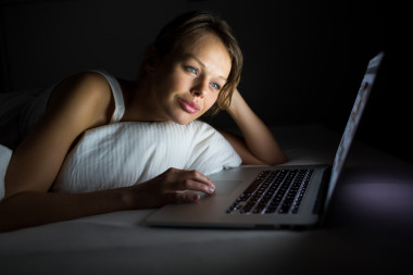 漂亮的年輕女人在床上用她的筆記本電腦