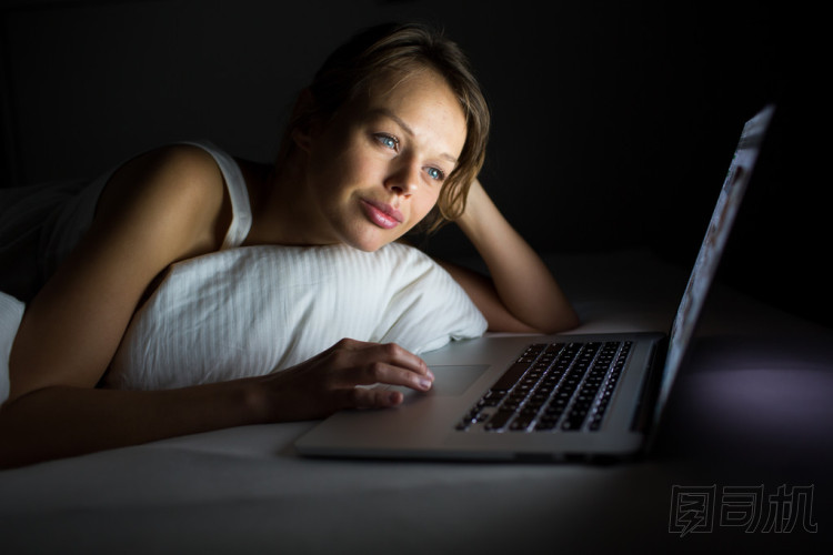 漂亮的年輕女人在床上用她的筆記本電腦