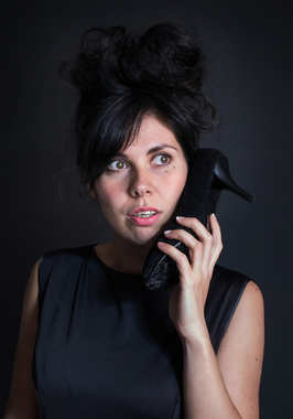 肖像照片的黑色裙与高的发型，拿着一双高跟鞋作为一个电话惊喜的女孩