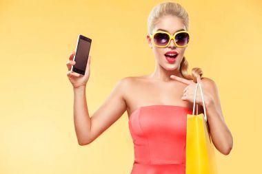 購物。年輕微笑的女子捧著袋子和手機(jī)在黑色星期五假期彌補(bǔ)她的拇指。在副本空間帶黃色背景上的女孩