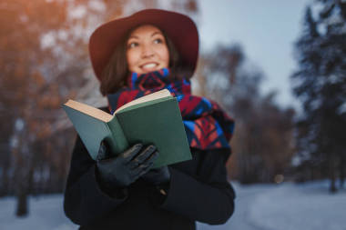 紅色帽子持有和閱讀詩歌書在冬季森林背景的年輕女子