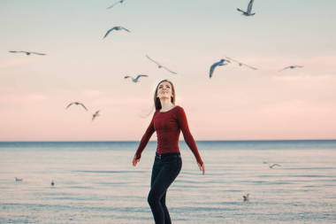 肖像的幸福的微笑笑興奮高加索運(yùn)行跳海鷗鳥(niǎo)群當(dāng)中日秋高氣爽的秋季戶外在岸灘上在日落，生活方式自然情感的牛仔褲的年輕女子