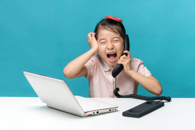 生氣，小女孩正坐在桌與她白色的筆記本電腦和一部電話，孤立在藍色的可愛亞洲