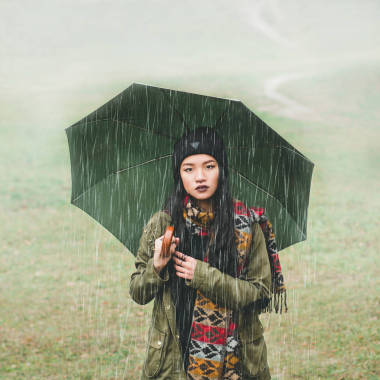 戲劇女孩打著傘，亞洲人的樣子。雨。一個(gè)女孩站在早期天氣場(chǎng)的背景中。形象總體規(guī)劃/中期規(guī)劃。女孩看著照相機(jī)