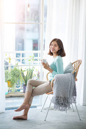 年轻漂亮的女人坐在打开的窗口，喝咖啡