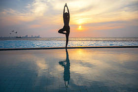 剪影年轻女人上练瑜伽的游泳池和海滩日落时分