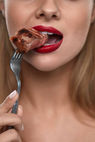 女人在吃肉。咬肉的美麗女性面部的特寫