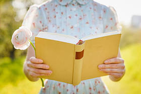 在春天公园举行本打开的书的女手的特写镜头。阅读概念背景