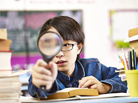 好奇的亚洲学生，拿着放大镜在一只眼睛