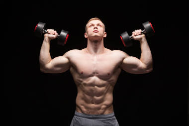 英俊的權(quán)力人健身模型與六包是訓(xùn)練與啞鈴，與 copyspace 的黑色背景上孤立