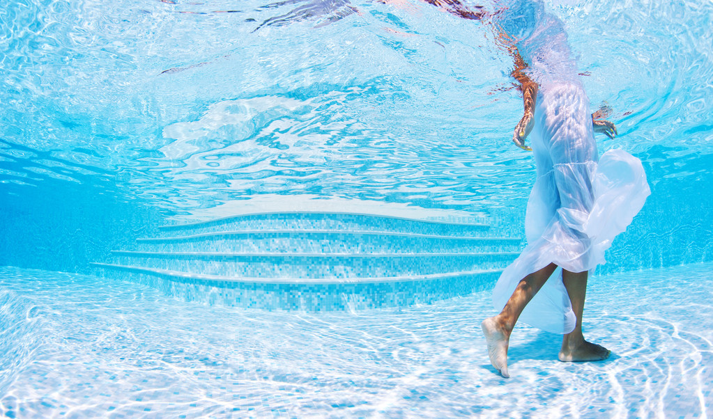 在游泳池中的白色礼服的水下女人时尚人像