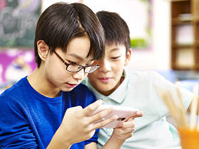 两名亚洲小学男生玩游戏用的手机