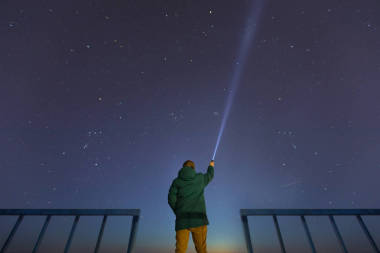 一個(gè)男人與一個(gè)手電筒，觀察美麗、 廣闊的藍(lán)色的夜空，星星與可見銀河系的輪廓。天文學(xué)、 取向、 晴朗的天空概念和背景