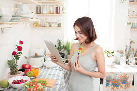 快乐漂亮的亚洲女子准备健康的食品，在厨房里和阅读使用数字平板的食谱