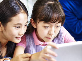 使用数字平板电脑在一起的两个亚洲小学女学生