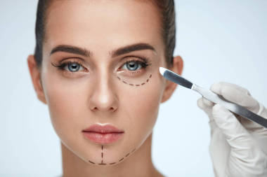 美容师手用手术刀靠近年轻女子的脸的特写