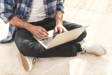 男人坐在地毯上，在笔记本上打字