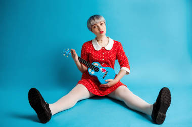 密切聯(lián)系穿件紅色的連衣裙，夏威夷四弦琴緩繳藍(lán)色背景光紫色短發(fā)的 dollish 美女畫(huà)像