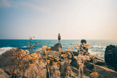 日落海灘上的男孩。這家伙孤獨地站在巖石，在海灘上