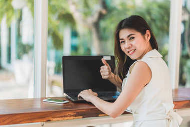 亚洲女人时的笑容用拇指上使用笔记本电脑