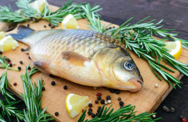 大活鯉魚 （鯽魚） 在與迷迭香樹枝的砧板上。新鮮的漁獲。關(guān)閉